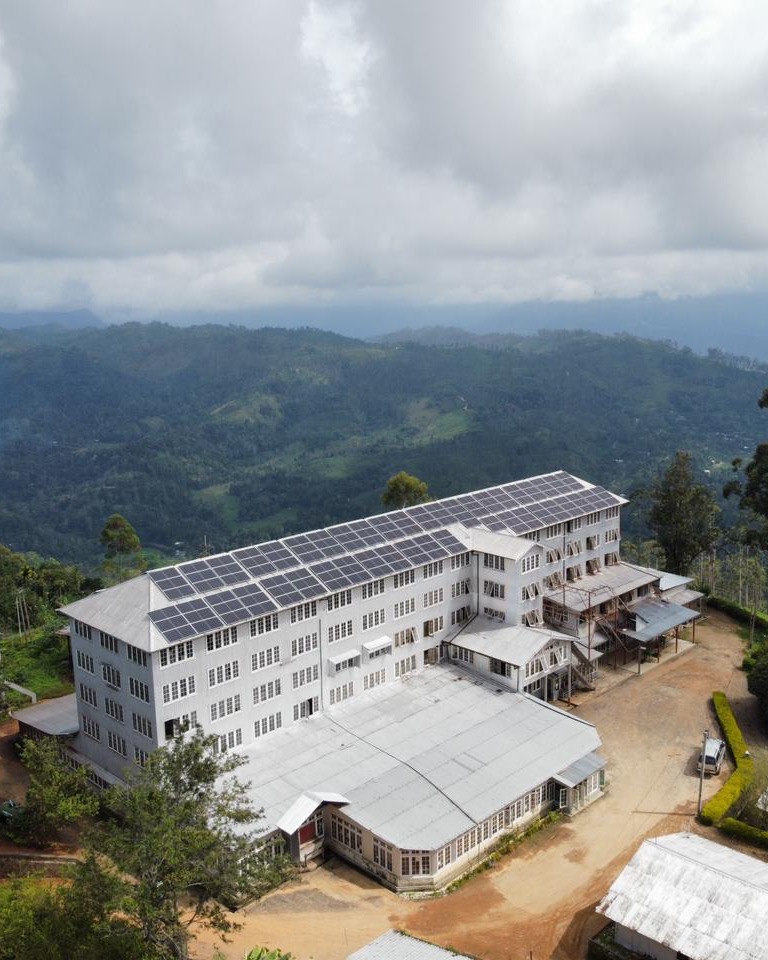 The Malwatte Valley factory on its ridge, solar panels across the roof, tea country behind it.